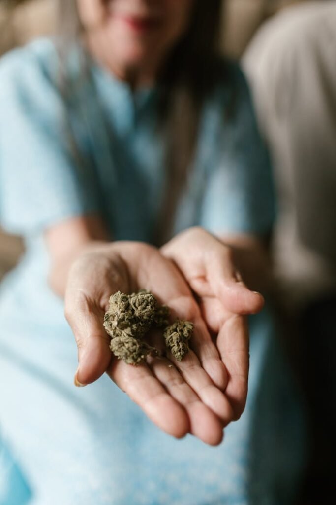 Close-up of individual holding dried cannabis buds in hands, blurred background.
